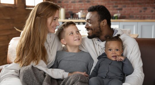 Eine Familie sitzt zusammen im Wohnzimmer als Symbol für die Vorteile der Niederlassungserlaubnis