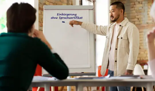 Ein Lehrer zeigt auf eine Tafel während ein Schüler aufmerksam guckt. Auf der Tafel steht Einbürgerung ohne Sprachtest