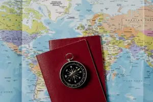 This picture shows a black compass on two national passports. The national passports are brown in color. In the background is a world map in different colors. A German passport is very valuable worldwide