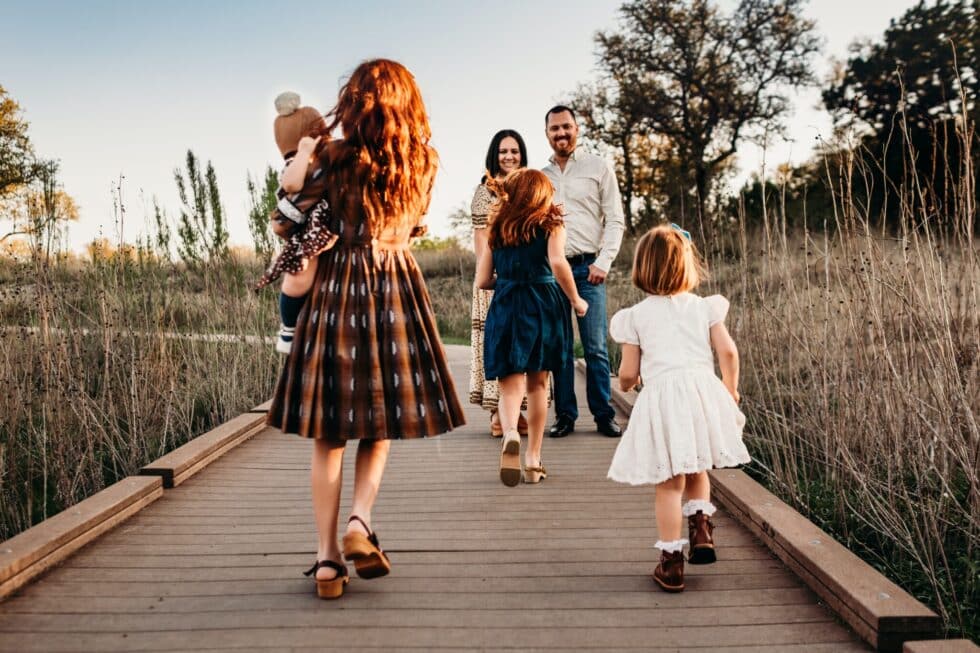 La imagen muestra a una familia en un puente. Los niños corren hacia sus padres. Al fondo, un paisaje verde.