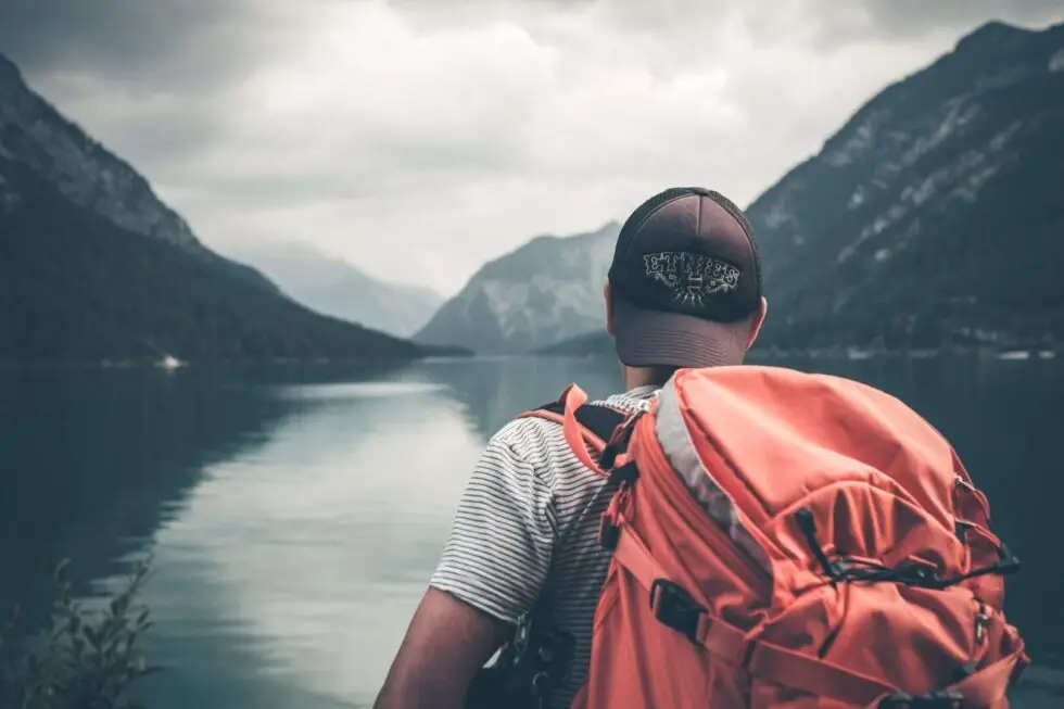 Auf dem Bild ist ein Mann mit Rucksack zu sehen. Er schaut auf einen See und auf ein Bergmassiv