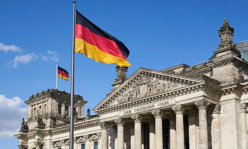 Auf dem Bild ist eine Deutschlandfahne vor dem Reichstagsgebäude in Berlin zu sehen. Der Himmel im Hintergrund ist blau