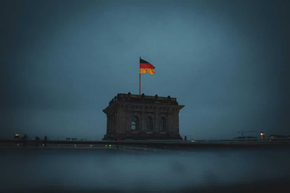 This picture shows a German flag on a building. The sky in the background is dark blue