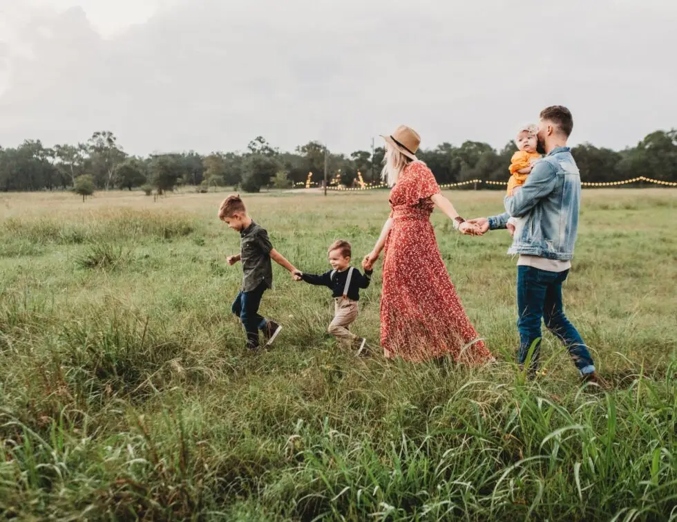 Auf diesem Bild sehen Sie eine Familie beim Spaziergang. Die Eltern und ihre Kinder laufen auf einer grünen Wiese