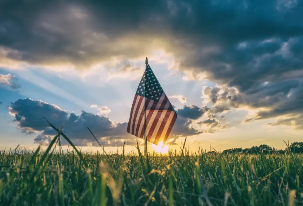 Auf diesem Bild sehen Sie eine US-Flagge auf einer grünen Wiese. Im Hintergrund befindet sich ein blauer Himmel