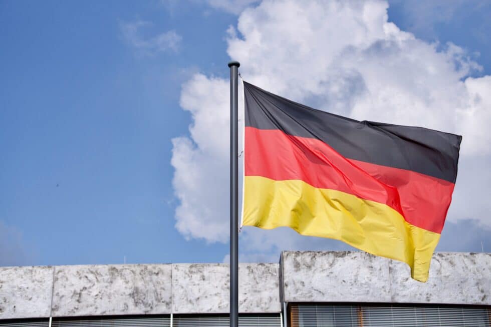 Auf diesem Bild sehen Sie eine deutsche Flagge vor einem Gebäude. Der Weg von der Fiktionsbescheinigung zur Einbürgerung ist nur auf Umwegen möglich.