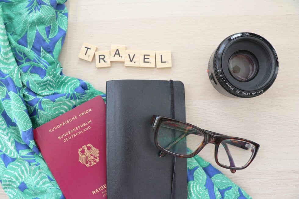 Na tym zdjęciu widać słowo Travel (wakacje) jako scrabble w literach scrabble. Obok znajduje się niemiecki paszport i para okularów.
