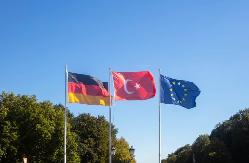 Auf diesem Bild sehen Sie die deutsche, die türkische und die EU-Flagge gemeinsam. Im Hintergrund befinden sich mehrere Bäume