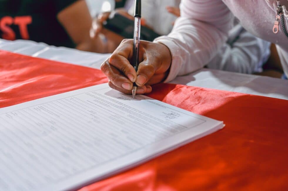 In this picture, a person is signing a document on a red cloth as a base.