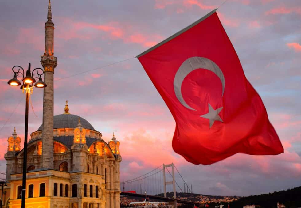 在这张照片中，您可以看到清真寺前的土耳其国旗。背景中可以看到日落