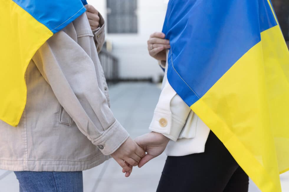 In this photo you can see two people each carrying a Ukrainian flag. The people are holding hands
