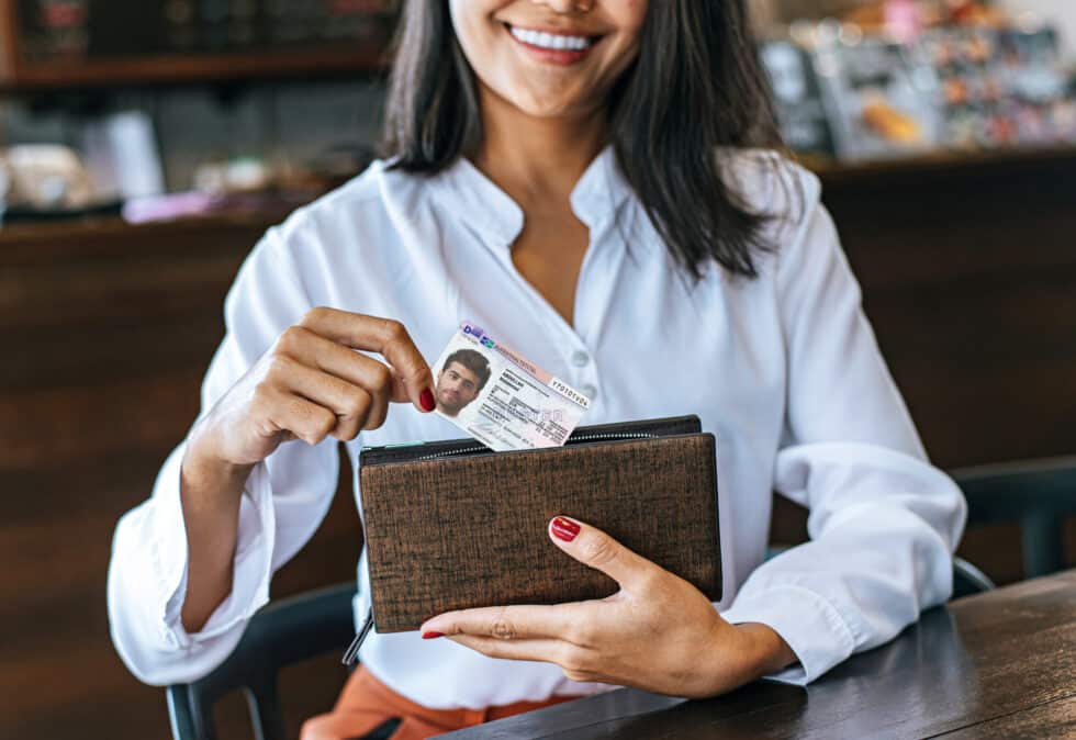 Auf diesem Bild zieht eine Frau einen Aufenthaltstitel mit einem männlichen Gesicht aus der Geldbörse