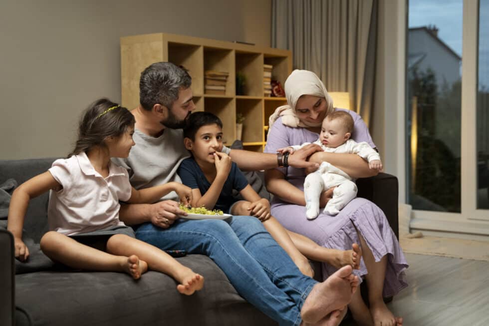 Auf diesem Bild sitzt eine muslimische Familie auf der Couch. Im Hintergrund befindet sich ein Regal