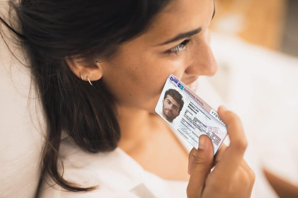 Auf diesem Foto hält eine Frau eine Karte von einem Aufenthaltstitel an der Wange