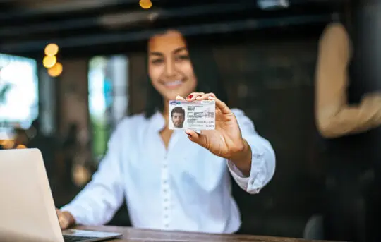 Eine Frau hält eine Karte mit dem Aufenthaltstitel § 25 Abs 2 zur Flüchtlingseigenschaft in der Hand.