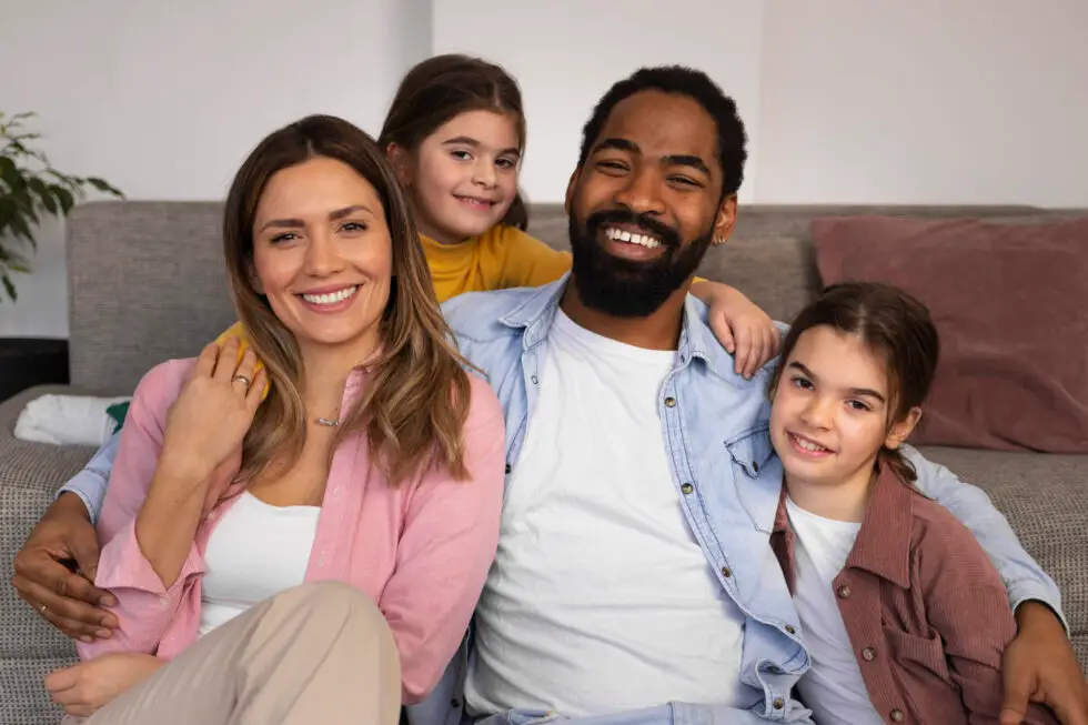 Auf diesem Foto sehen Sie glückliche Eltern mit ihren Kindern zuhause. Die Familie sitzt auf einem Sofa