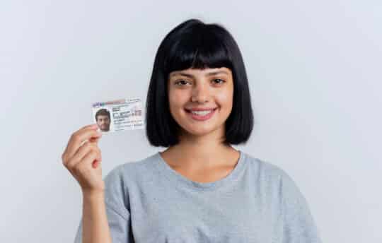 Auf diesem Foto hält eine lächelnde junge Frau eine Karte mit dem Aufenthaltstitel Paragraf 19c AufenthG in der Hand