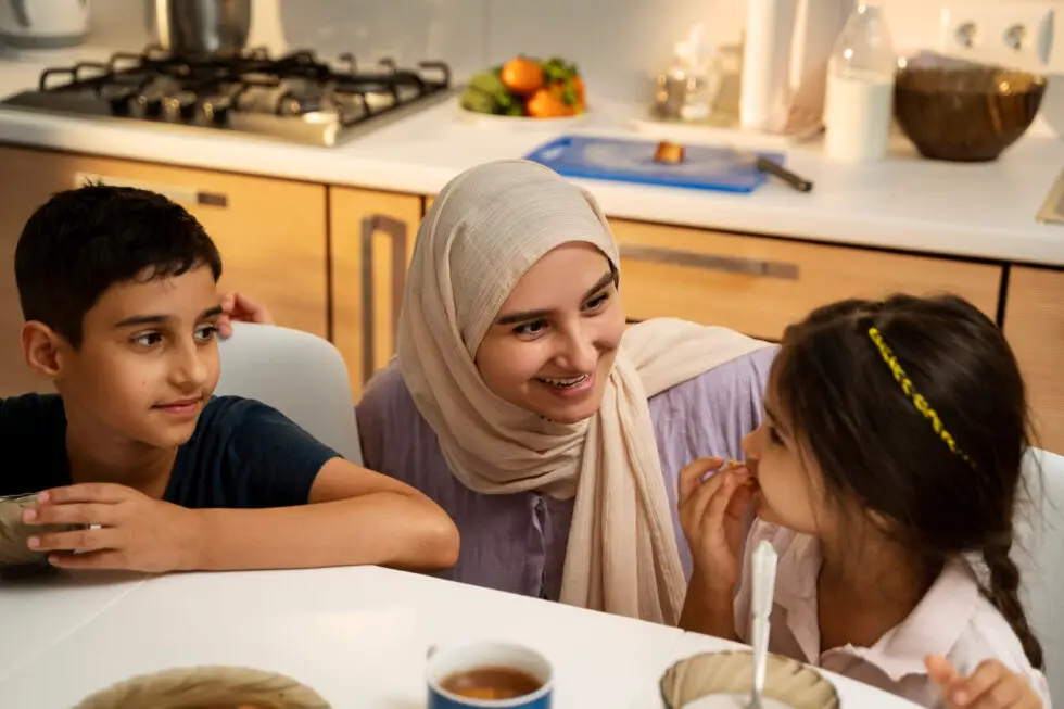 Sur cette photo, on voit une mère musulmane avec des enfants à table. En arrière-plan, une cuisine avec une cuisinière.