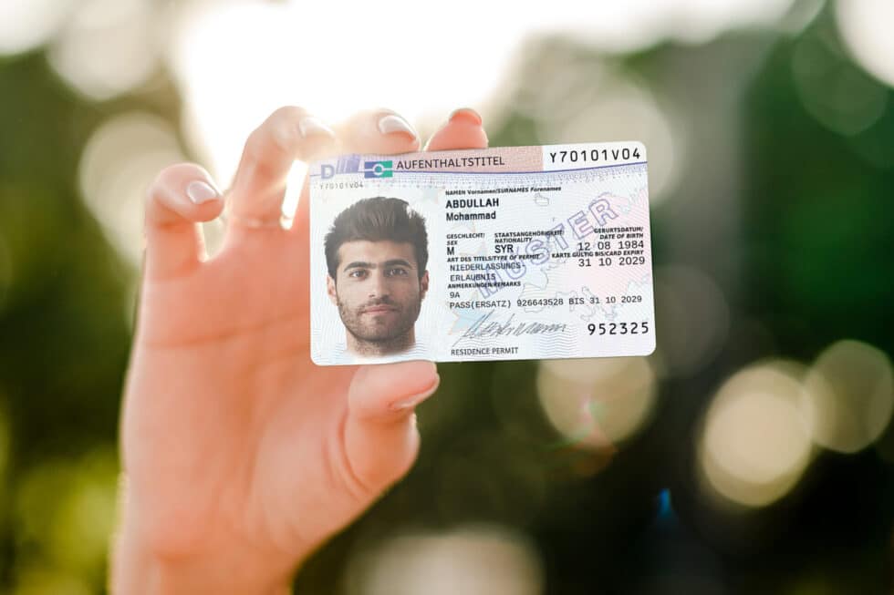 Eine Person hält eine Karte zur Niederlassungserlaubnis in die Kamera