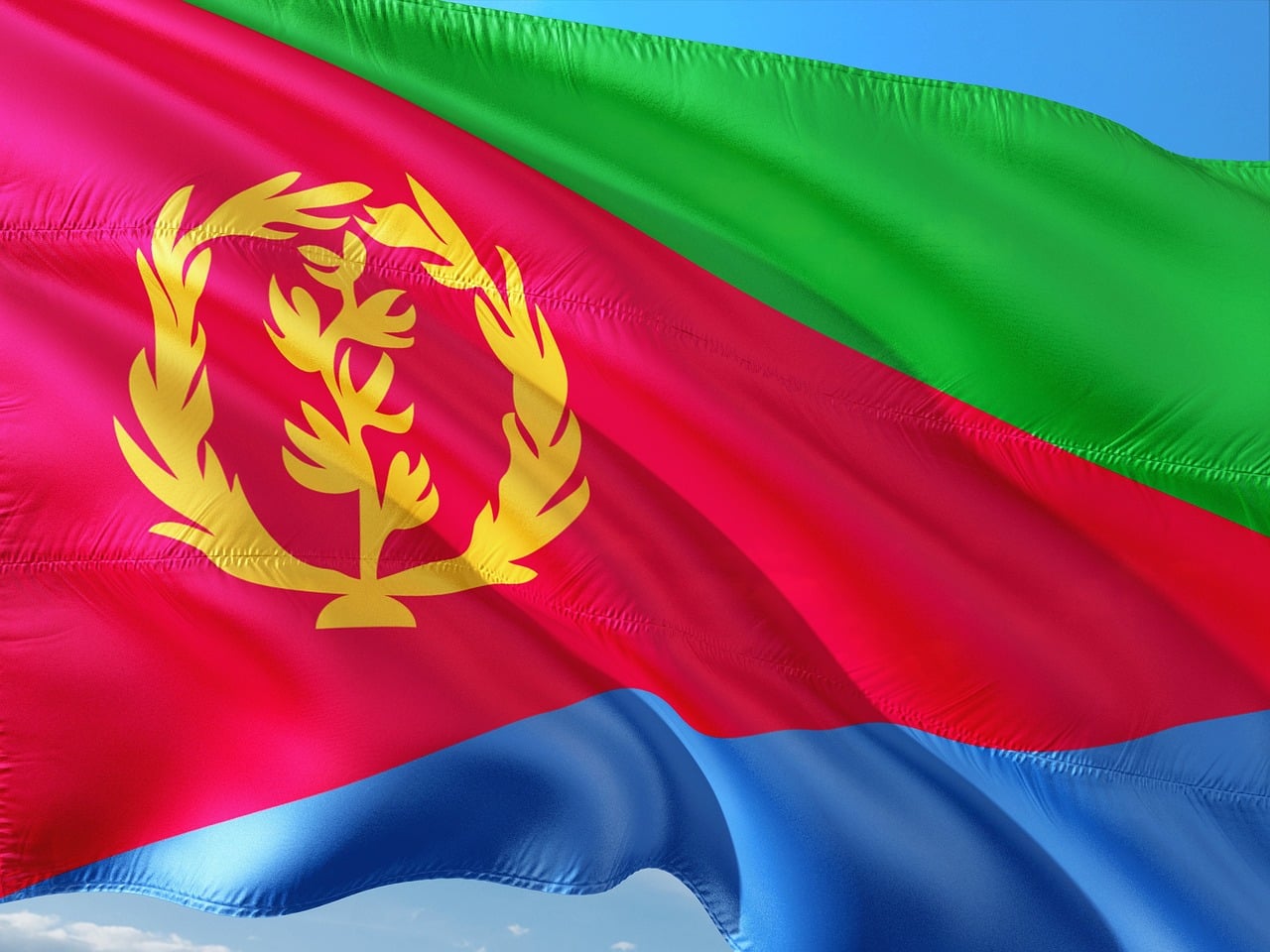 Flagge von Eritrea mit einem grünen Dreieck entlang des Mastes und roten, blauen und grünen horizontalen Streifen, überlagert von einem goldfarbenen Olivenzweig-Kranz in der Mitte.
