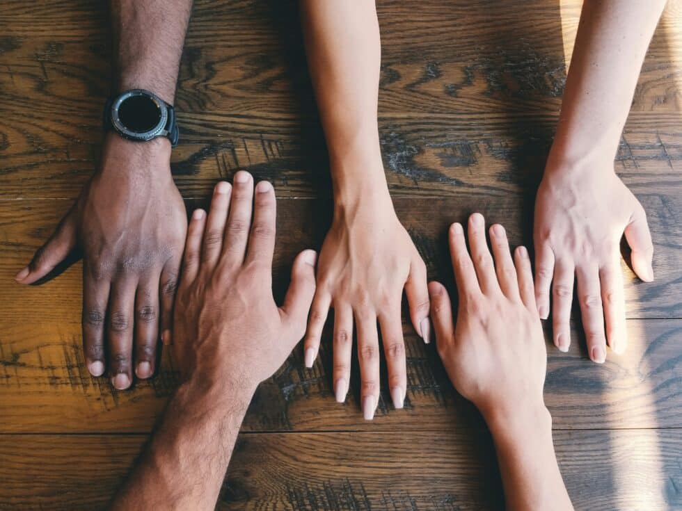 Hands of different skin colors lie next to each other on a wooden table, symbolizing integration and the naturalization process in a multicultural society.