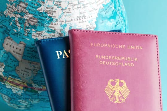 Two passports, one with the inscription &#039;European Union Federal Republic of Germany&#039; and the other with just &#039;Passport&#039;, lie on a globe with a focus on Europe, symbolizing dual citizenship.