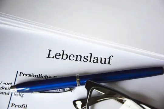 Ein aufgeschlagener Lebenslauf mit einem blauen Stift und einer Brille darauf, symbolisch für die sorgfältige Vorbereitung eines Lebenslaufs zur Einbürgerung.