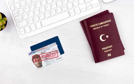 土耳其护照旁的过期居留证，放在桌子上，背景是键盘。居留证上盖有 &quot;EXPIRED（过期）&quot;印章。如果您的居留许可已无限期过期，您可以在此了解如何转移护照和更新文件。