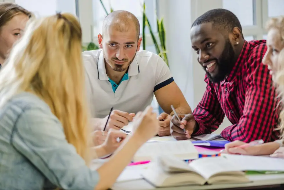 Eine Gruppe von Menschen unterschiedlicher Herkunft diskutiert und teilt Ideen an einem Tisch voller Bücher und Notizen. Diese Szene symbolisiert die Vorbereitung auf den Einbürgerungstest und die Bedeutung des Einbürgerungstest Zertifikats für die Integration in die deutsche Gesellschaft.