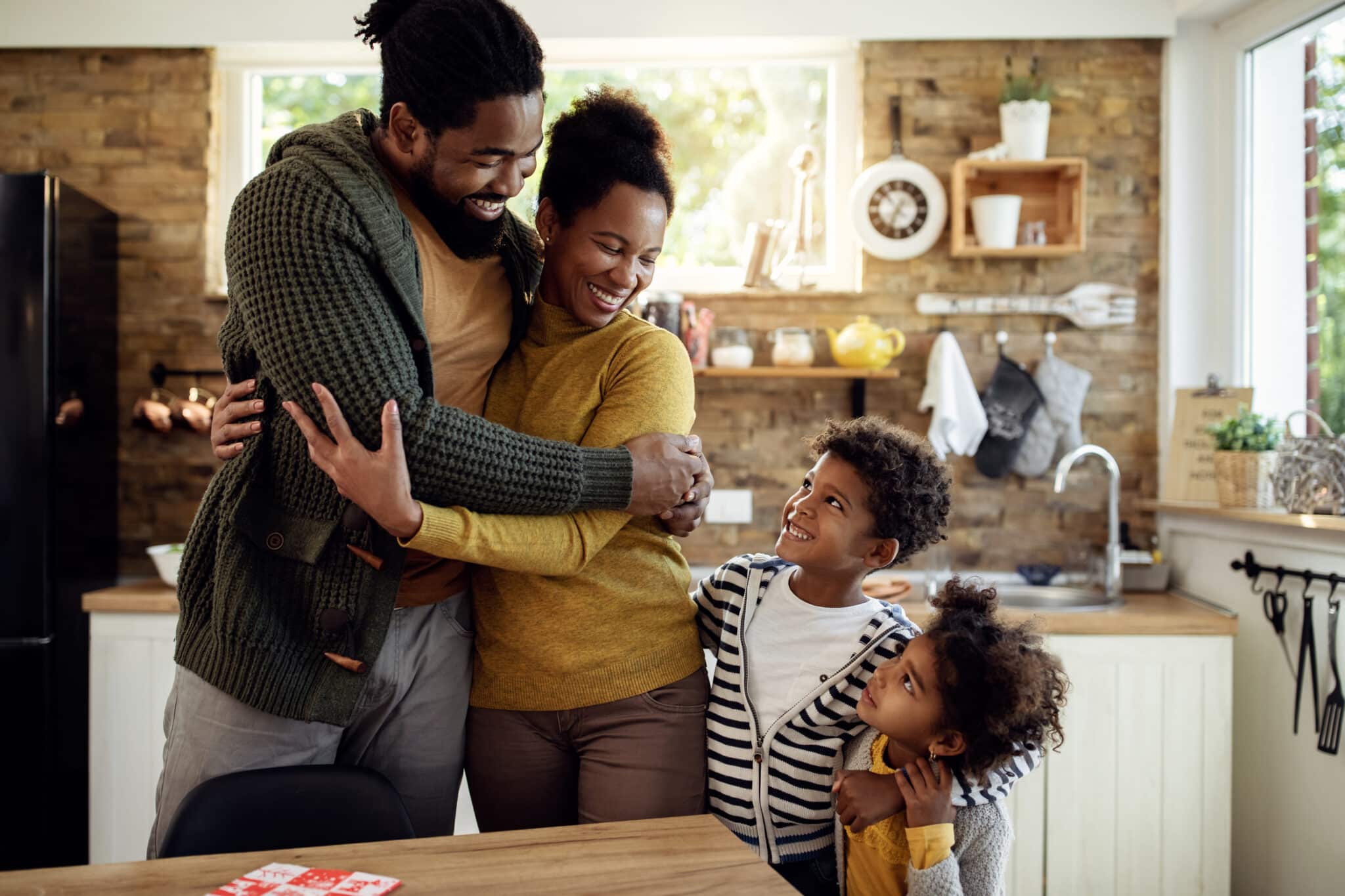 Eine glückliche Familie mit zwei Kindern umarmt sich und lächelt in ihrer gemütlichen Küche. Dieses Bild veranschaulicht die Vorteile und das Ziel des Familiennachzugs gemäß § 28 AufenthG.