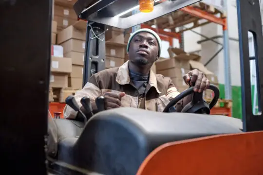 Ein Auszubildender in einem Lager fährt einen Gabelstapler und arbeitet konzentriert. Dieses Bild symbolisiert eine handwerkliche oder logistische Ausbildung, die durch die Berufsausbildungsbeihilfe (BAB) unterstützt werden könnte. Der Bezug zur Ausbildung und zur Sicherung des Lebensunterhalts wird deutlich, was im Zusammenhang mit der Einbürgerung in Deutschland von Bedeutung ist.