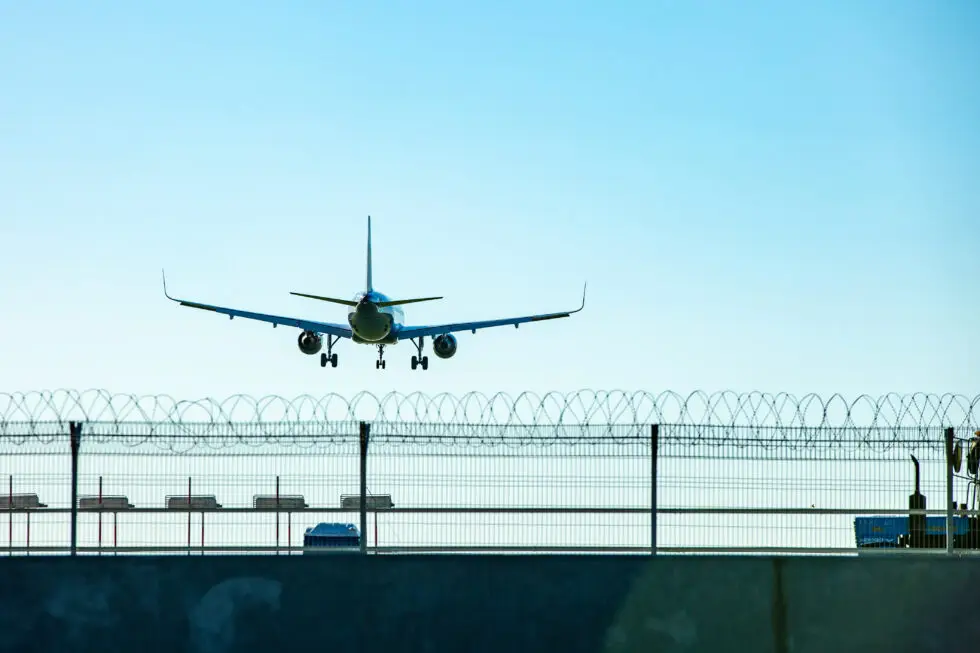 Ein Flugzeug hebt ab hinter einem mit Stacheldraht gesicherten Zaun, symbolisch für Ausweisungen gemäß § 53 AufenthG und die damit verbundenen rechtlichen und persönlichen Herausforderungen im Bereich Ausweisung und Bleiberecht.