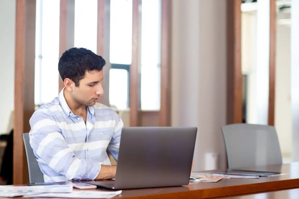 Ein junger Mann sitzt in einem Büro und arbeitet an seinem Laptop. Er recherchiert zu § 53 AufenthG und den Themen Ausweisung und Bleiberecht, um sich über die rechtlichen Bestimmungen zu informieren.