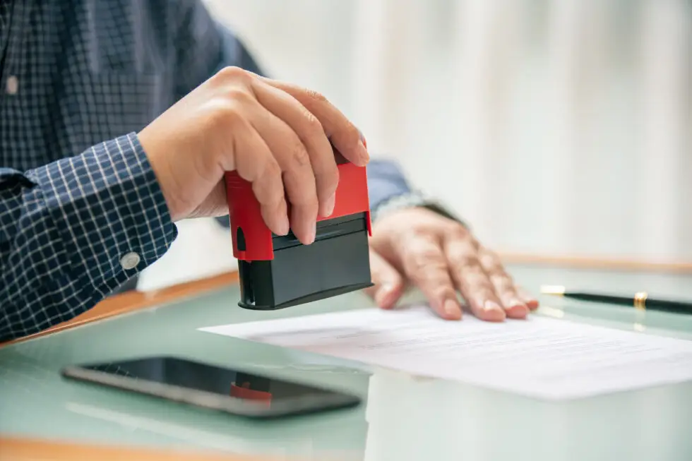 in Mann stempelt ein Dokument ab, was den Abschluss eines bürokratischen Prozesses symbolisiert. Dies steht im Zusammenhang mit der Zustimmung der Bundesagentur für Arbeit gemäß § 39 AufenthG, die oft erforderlich ist, um eine Arbeitserlaubnis für ausländische Arbeitnehmer in Deutschland zu erteilen.