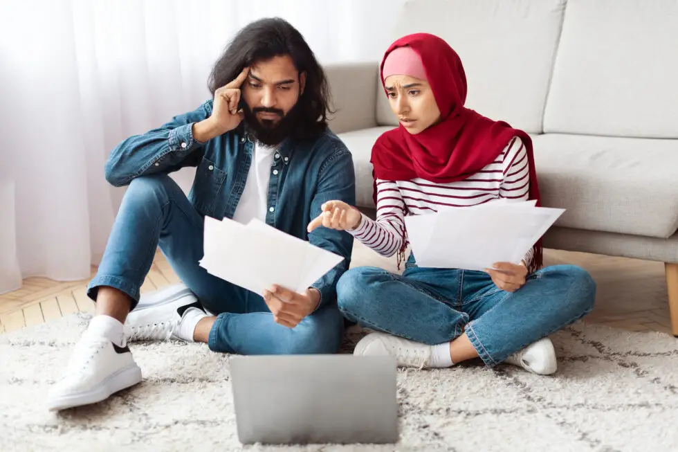 Jeune couple assis par terre, vérifiant ensemble des documents - symbole de la préparation et du processus de demande de naturalisation en Allemagne en 2024. L'image reflète le rôle important des documents et de la coopération dans le processus de demande de citoyenneté.