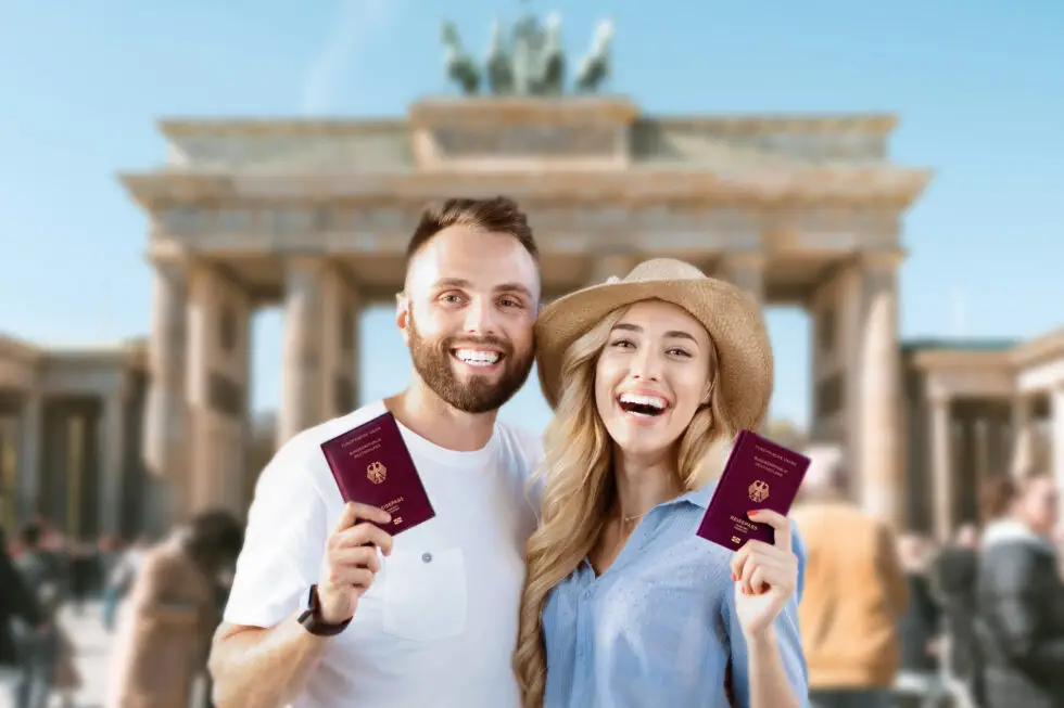 Sur cette photo, vous voyez un couple heureux avec un passeport allemand devant la porte de Brandebourg. En rapport avec le thème Naturalisation Allemagne