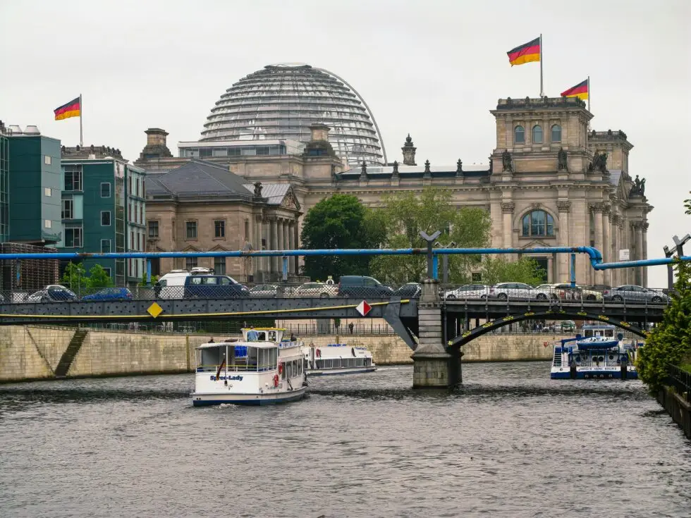 Das Reichstagsgebäude in Berlin samt gläserner Kuppel. Im Vordergrund fährt ein Tiuristenboot die Spree hinunter. Steht der Familiennachzug für subsidiär Schutzberechtigte vor dem Aus? Aktuell diskutiert die Bundesregierung genau darüber. Die Entscheidung soll noch vor der Sommerpause fallen.