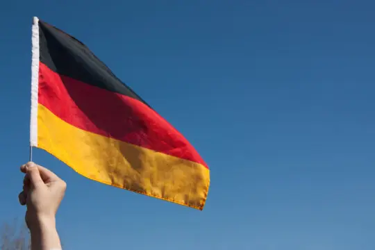 Auf dem Bild sehen Sie eine Hand, die die deutsche Flagge hochhält. Laut einer DIW-Studie streben immer mehr Geflüchtete die deutsche Staatsbürgerschaft an oder haben diese bereits erhalten.