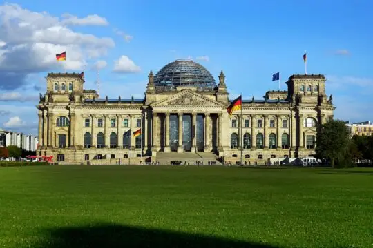 Das Bild zeigt den deutschen Reichstag mit der gläsernen Kuppel und der deutschen Flagge. Turbo-Einbürgerung, Asyl und die Einstufung sicherer Herkunftsländer. Der Bundestag berät über verschiedene migrationsplotische Themen.
