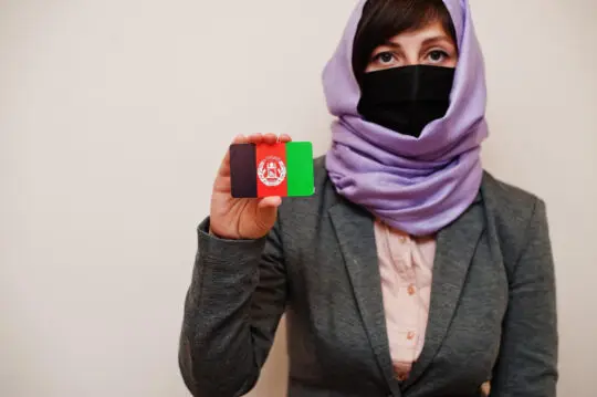 Das Bild zeigt eine afghanische Frau, die eine Karte mit der Flagge von Afghanistan hochhält. Seit Anfang Oktober leiten Vertreter der Taliban das afghanische Konsulat in Bonn. Damit haben sie potenziell auch Zugriff auf zahlreiche personenbezogene Daten von Afghanen und Afghaninnen in Deutschland.